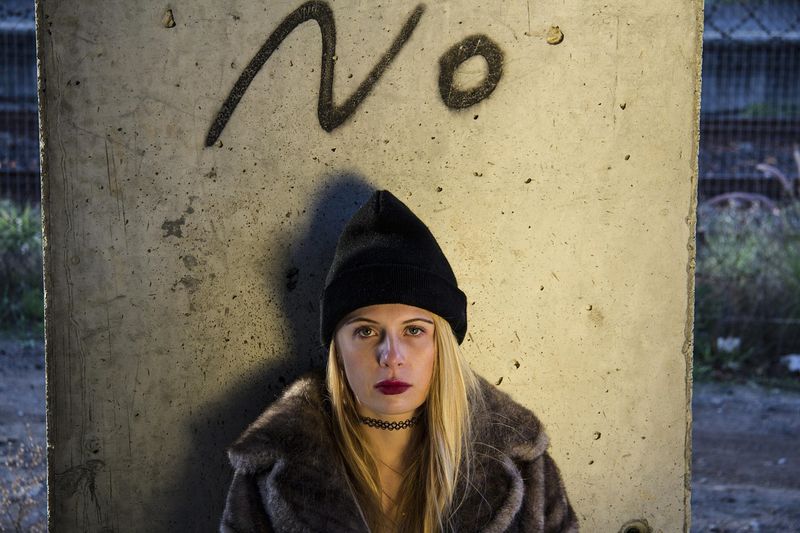 Junge Frau mit Mütze lehnt an einer Betonwand, über ihr der Schriftzug „No“