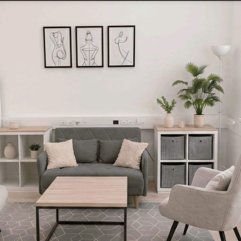 Heller Beratungsraum mit grauem Sofa, Sessel, Couchtisch, Pflanzen und drei Linienzeichnungen an der Wand