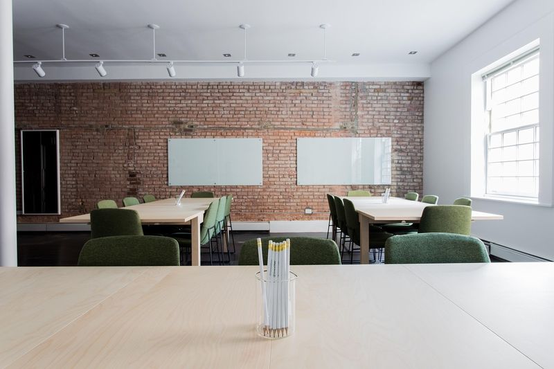 Heller Seminarraum mit Ziegelwand, großen Fenstern, Tischen und Whiteboard
